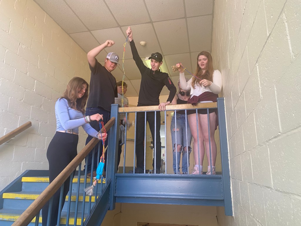 Students collaborating on a project by the staircase, using strings and materials to create experiments or demonstrations.